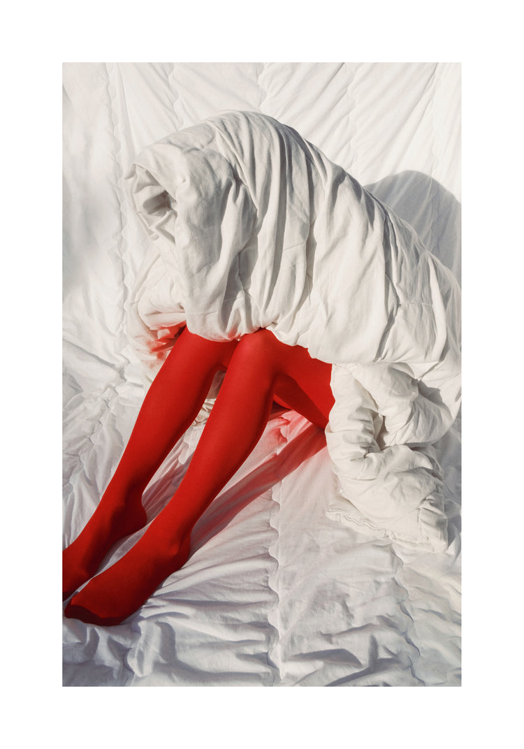 Woman in bright red stockings covered in a thick white down blanket.
