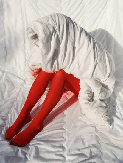 Woman in bright red stockings covered in a thick white down blanket.