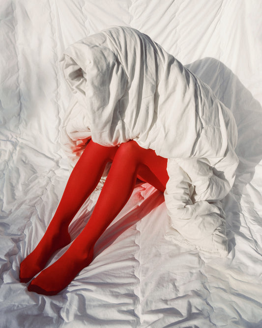 Woman in bright red stockings covered in a thick white down blanket.