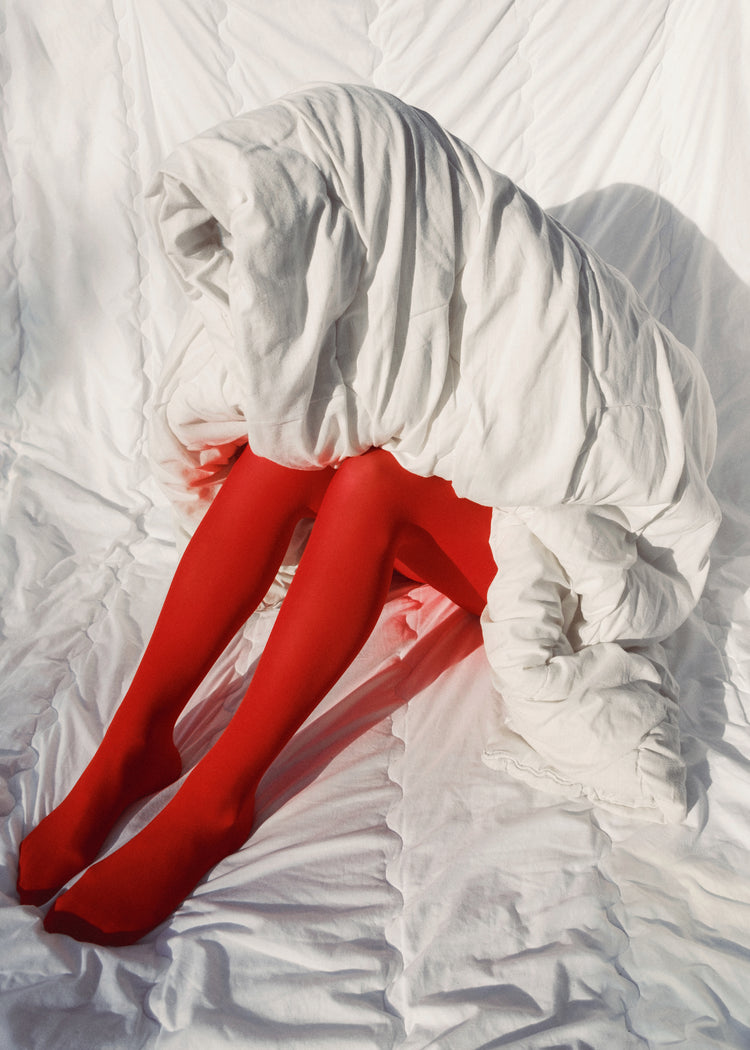 Woman in bright red stockings covered in a thick white down blanket.