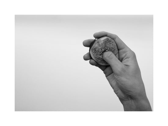 A hand holding half a fig and squeezing its flesh.