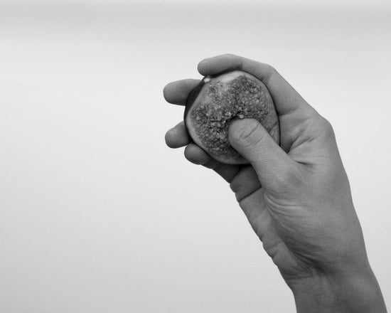 A hand holding half a fig and squeezing its flesh.