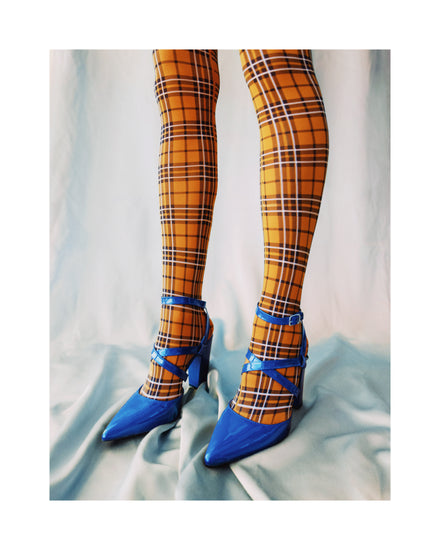 Legs wearing checkered mustard yellow stockings and high heeled blue sandals.