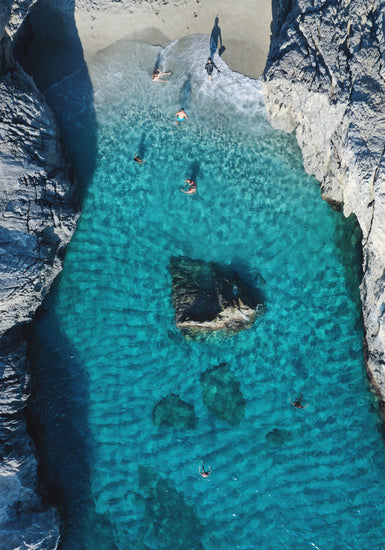 Turquoise natural pool between two cliff walls with people playing by the shore.