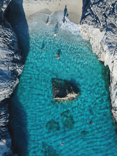 Turquoise natural pool between two cliff walls with people playing by the shore.