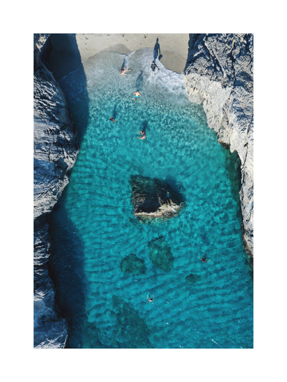 Turquoise natural pool between two cliff walls with people playing by the shore.