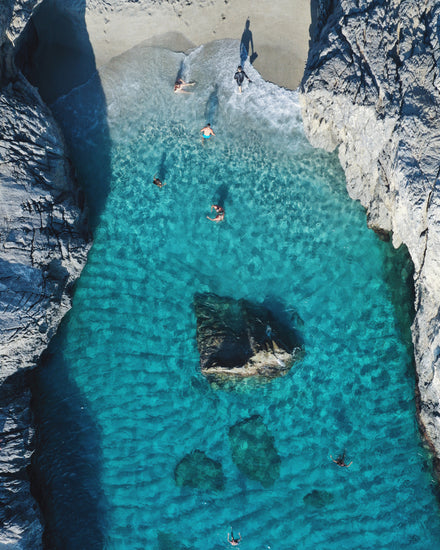 Turquoise natural pool between two cliff walls with people playing by the shore.