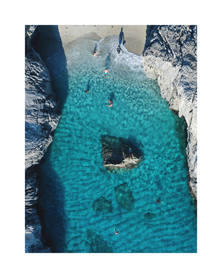 Turquoise natural pool between two cliff walls with people playing by the shore.