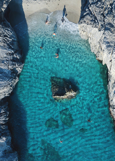 Turquoise natural pool between two cliff walls with people playing by the shore.