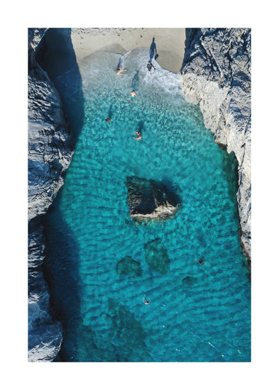 Turquoise natural pool between two cliff walls with people playing by the shore.
