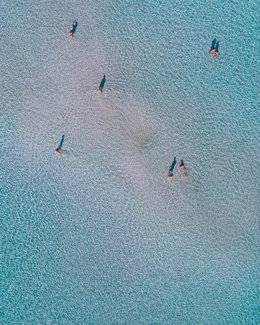 Drone footage of shallow blue waters and people swimming in it.