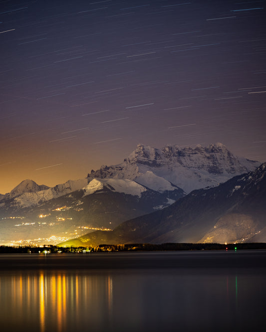 Star strewn sky above a city located next to a lake in the mountains.