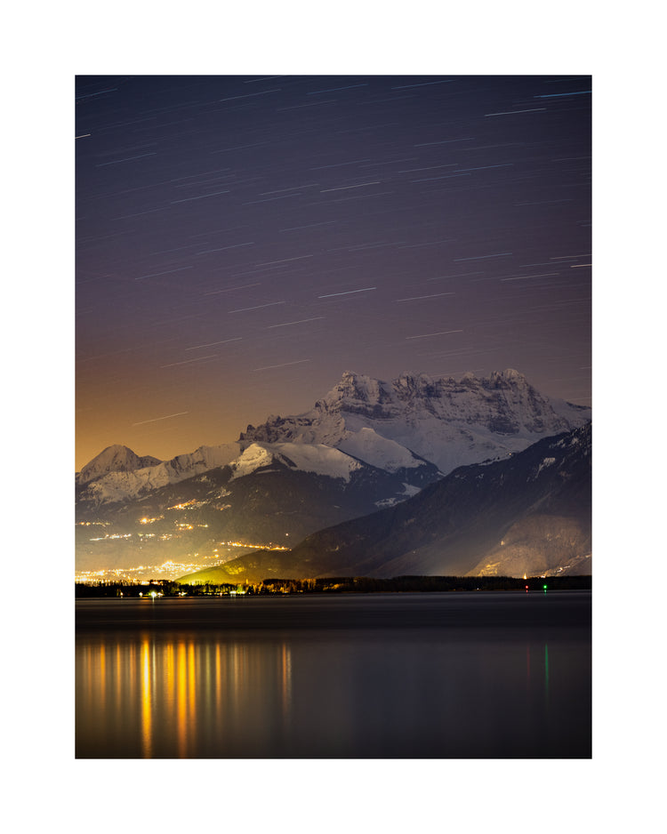 Star strewn sky above a city located next to a lake in the mountains.