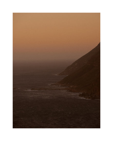 Coastline with a mountain towering along the shoreline during sunrise.