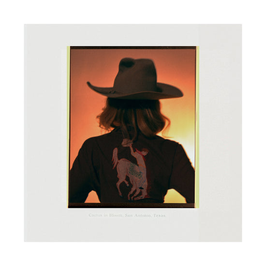 A woman with short hair and a cowboy hat dressed in a jacket with a cowboy print.