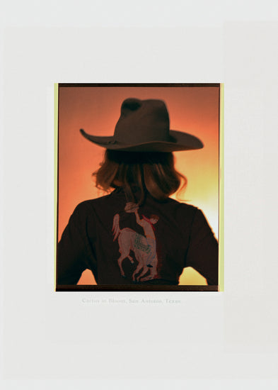 A woman with short hair and a cowboy hat dressed in a jacket with a cowboy print.