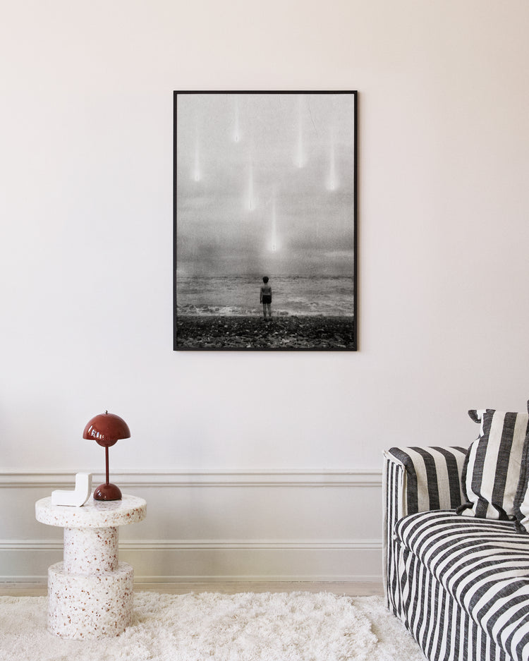 A modern living room showcases the Doubts Poster, a black-and-white photograph of a child facing the ocean with sky lights. The room features a striped sofa, small terrazzo table, and red lamp.
