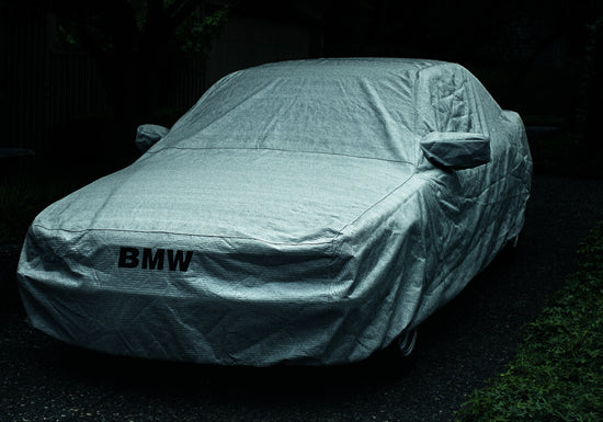 BMW car covered in a white sheet standing on a dark driveway.