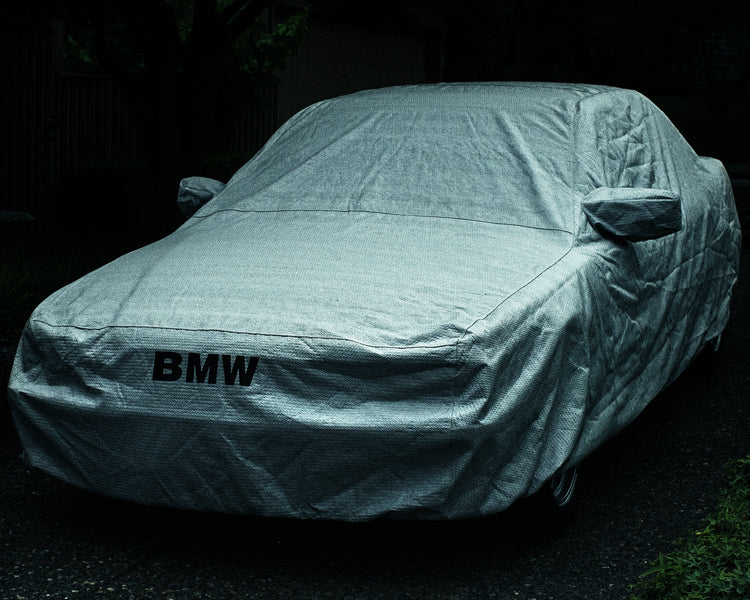 BMW car covered in a white sheet standing on a dark driveway.