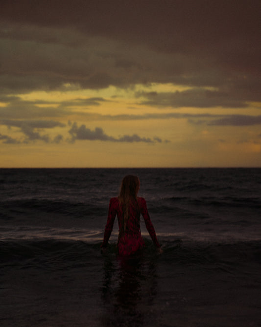 A woman in a red dressing gown walking into the ocean during sunset.
