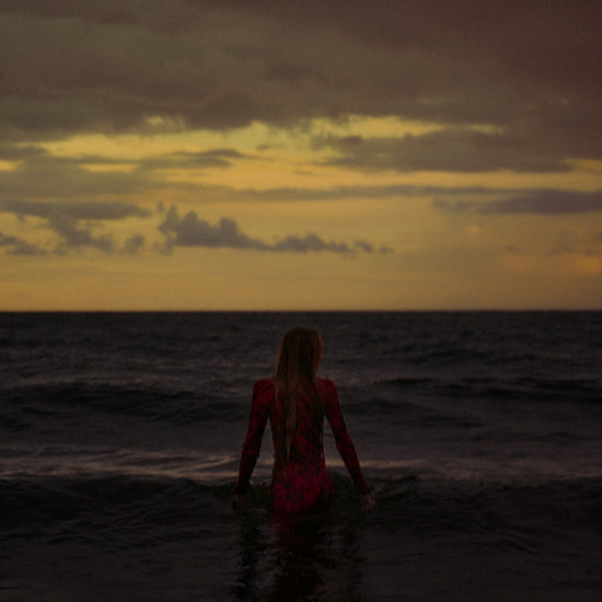 A woman in a red dressing gown walking into the ocean during sunset.