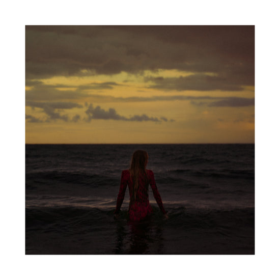 A woman in a red dressing gown walking into the ocean during sunset.