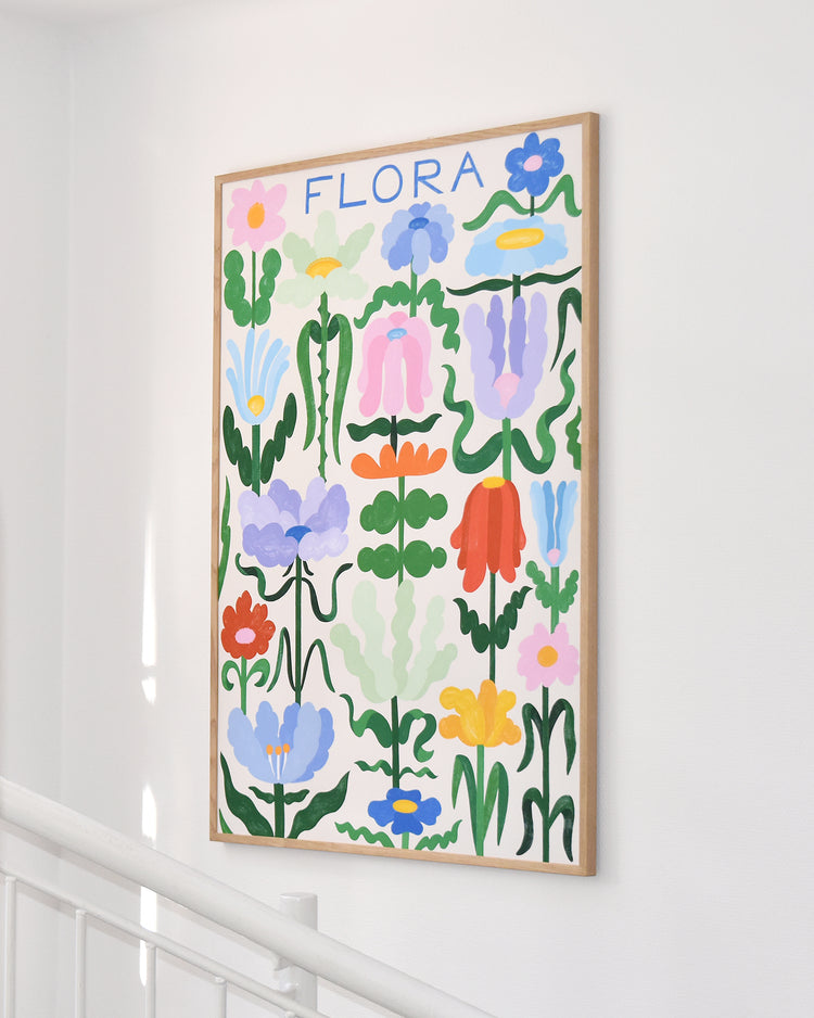 The Flora on White Poster showcases vibrant abstract flowers in various shapes and colors with elegant handwritten typography, hanging on a white wall above a staircase railing.