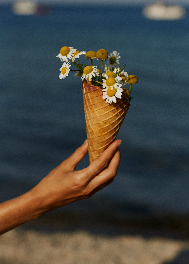 Ice cream cone full of white flowers in front of a blue sea.