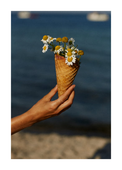 Ice cream cone full of white flowers in front of a blue sea.