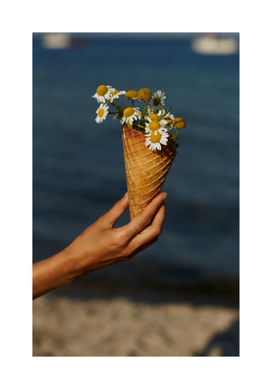 Ice cream cone full of white flowers in front of a blue sea.