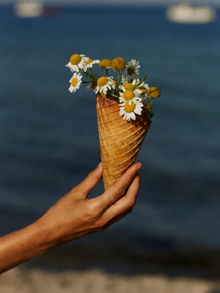Ice cream cone full of white flowers in front of a blue sea.
