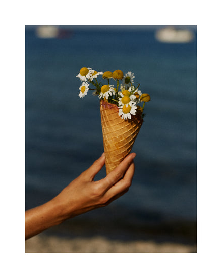 Ice cream cone full of white flowers in front of a blue sea.