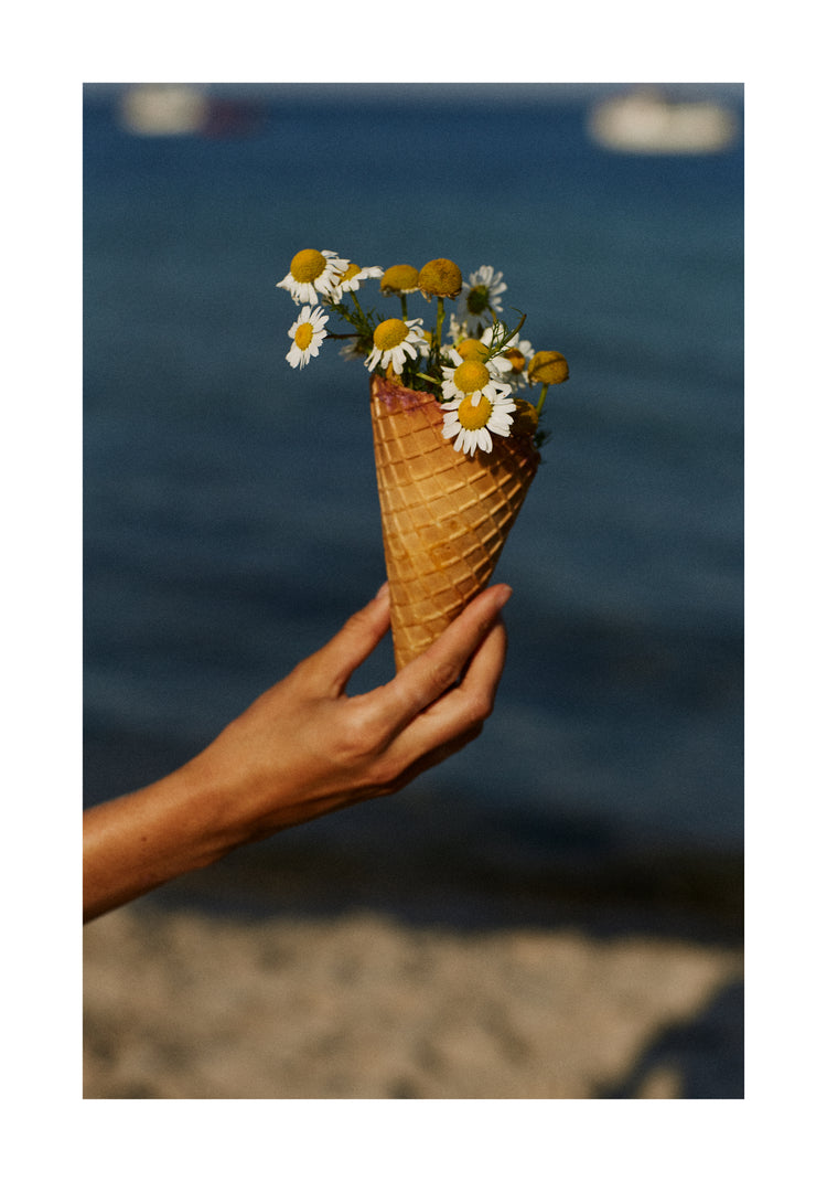Ice cream cone full of white flowers in front of a blue sea.