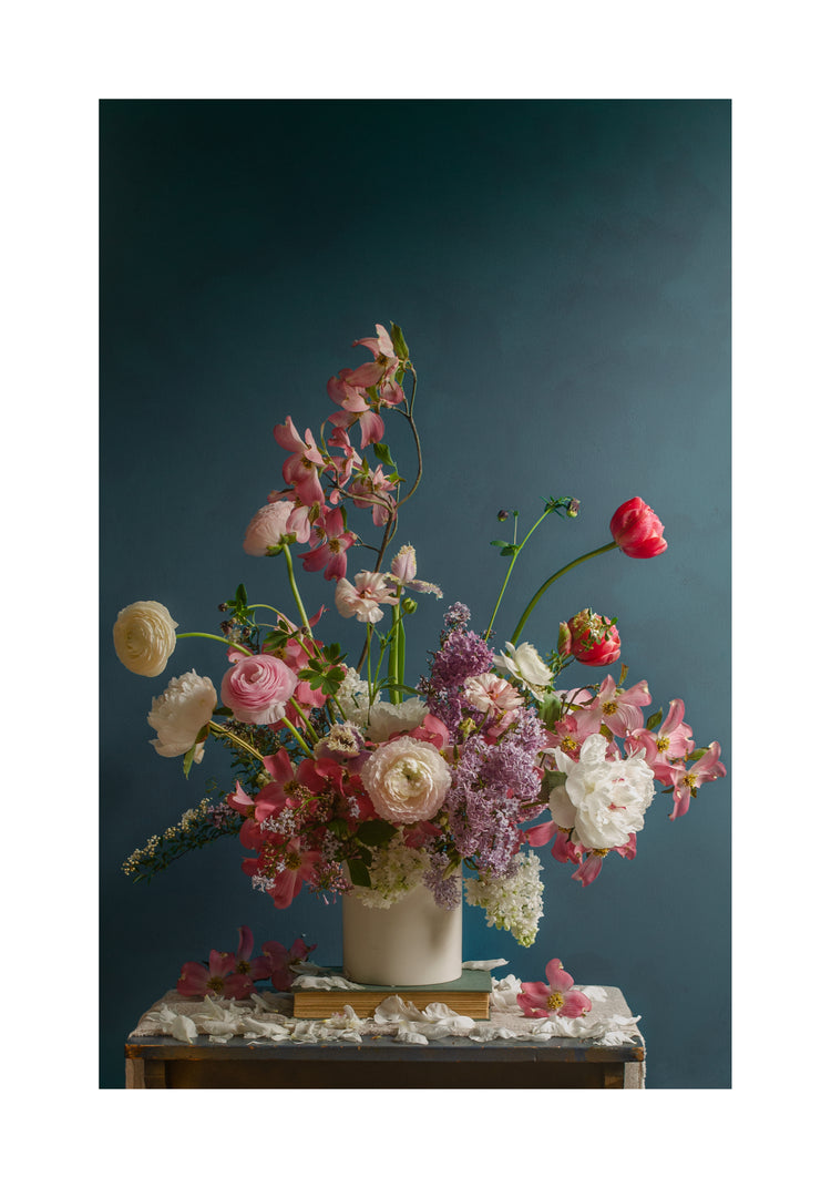 The Spring Ballet Poster depicts a vibrant floral arrangement with pink roses, white peonies, lilac clusters, and a red poppy in a white vase against a deep green backdrop, all set on a small table draped with a white cloth.