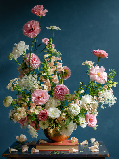 The Midsummer Poster features a lush bouquet of pink, white, and blush flowers such as roses, peonies, and wildflowers in a gold vase set against a dark teal background with scattered petals below.
