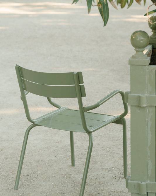 An Asseyez-vous Poster features a green metal chair on a sandy path under a tree, near a post, evoking a tranquil park setting with gentle natural lighting.