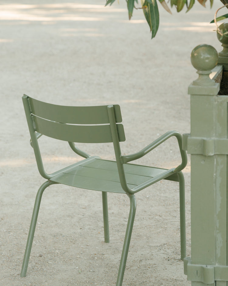 An Asseyez-vous Poster features a green metal chair on a sandy path under a tree, near a post, evoking a tranquil park setting with gentle natural lighting.