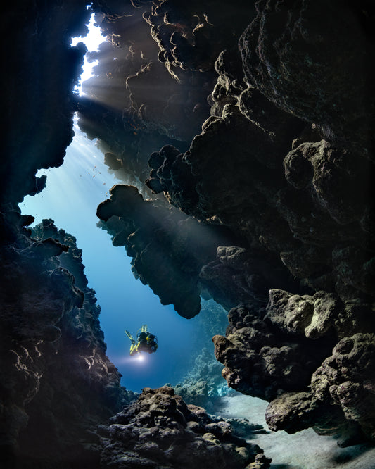 Diver swimming in the gap between cliff walls deep down in the ocean.