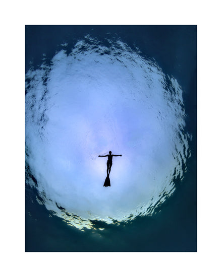 Diver floating underneath the surface of the sea captured from underneath.