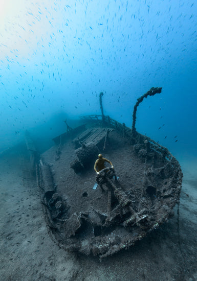 Shipwreck on the bottom of a deep blue ocean with a diver behind the wheel.