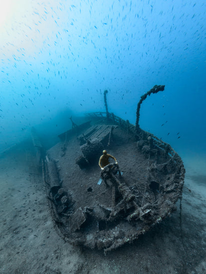 Shipwreck on the bottom of a deep blue ocean with a diver behind the wheel.