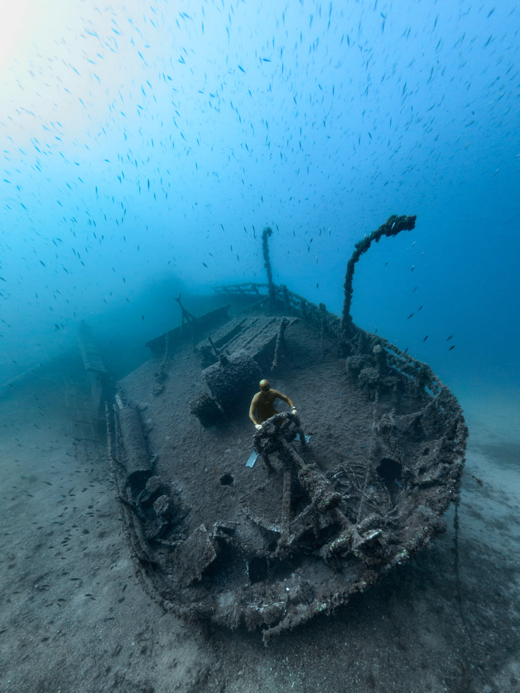 Shipwreck on the bottom of a deep blue ocean with a diver behind the wheel.