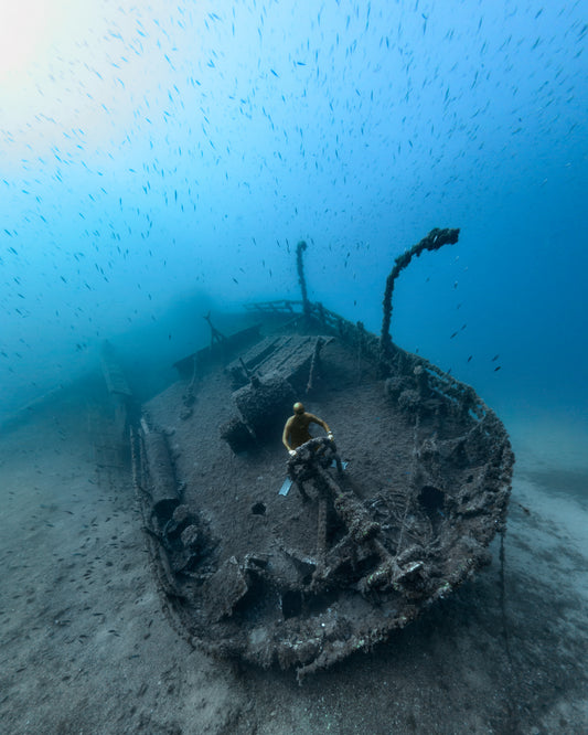 Shipwreck on the bottom of a deep blue ocean with a diver behind the wheel.