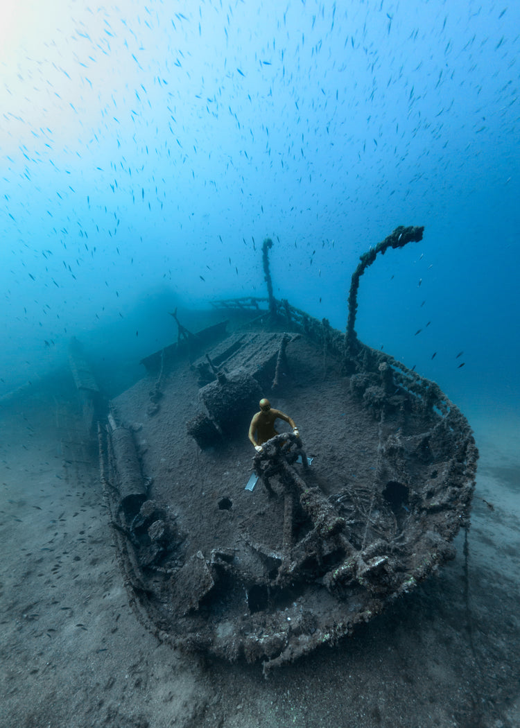 Shipwreck on the bottom of a deep blue ocean with a diver behind the wheel.