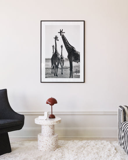 A modern living room with a black chair, terrazzo side table featuring a red lamp and book, the What Are You Waiting For? poster, ideal for unwinding after exercise. It includes a white fluffy rug and part of a striped chair.