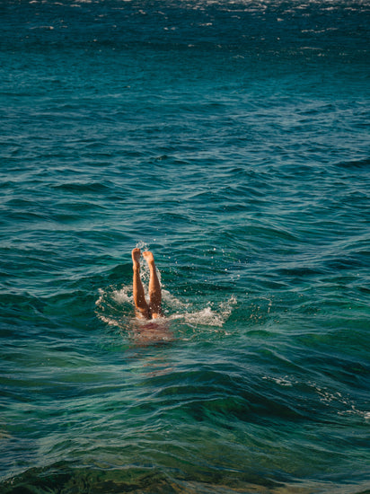 Legs of a person diving into the sea with their torso under the water’s surface.