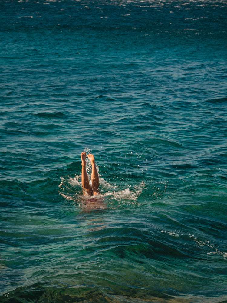 Legs of a person diving into the sea with their torso under the water’s surface.