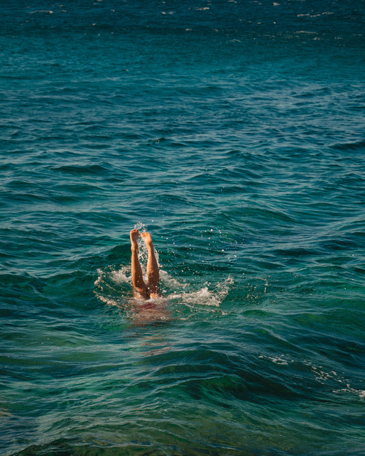 Legs of a person diving into the sea with their torso under the water’s surface.