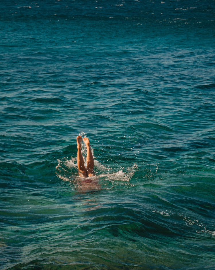 Legs of a person diving into the sea with their torso under the water’s surface.
