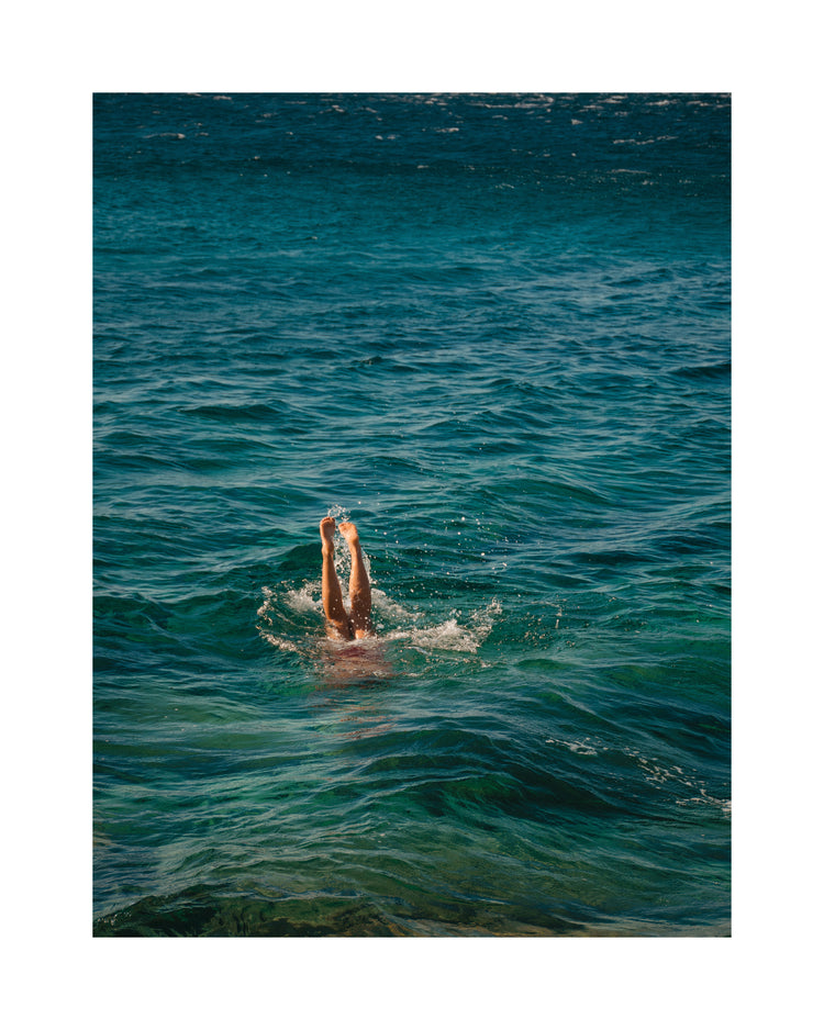 Legs of a person diving into the sea with their torso under the water’s surface.